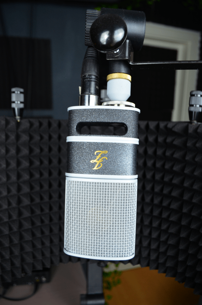 Close-up of a JZ V67 microphone with a soundproofing shield in the background, set up in a studio environment